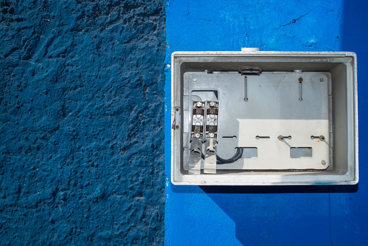 services-02 A weathered electrical panel on a vivid blue wall, blending industrial and artistic elements.